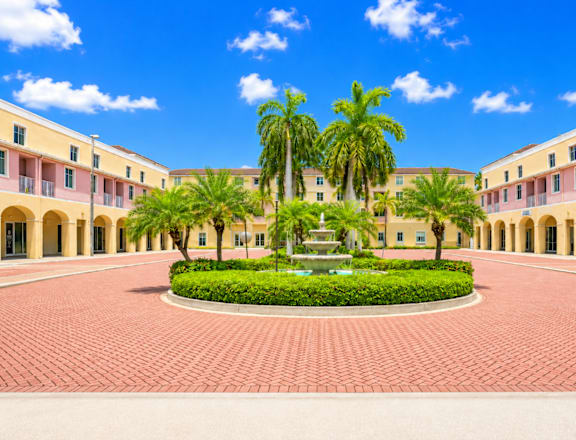 A courtyard with a fountain surrounded by palm trees and buildings.