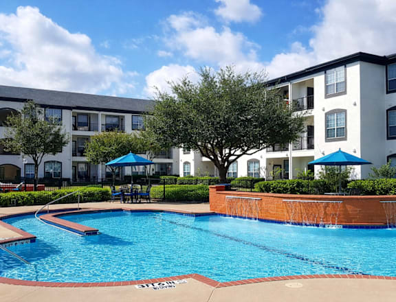 A swimming pool in front of a white apartment building.