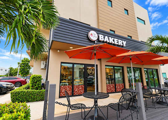 A bakery with a red umbrella and chairs outside.