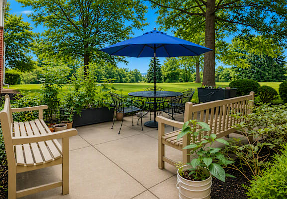 A blue umbrella sits in the middle of a patio with two chairs and a table.