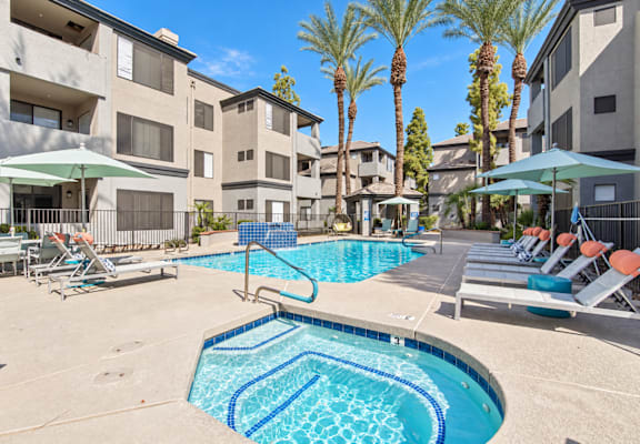 A swimming pool surrounded by lounge chairs and umbrellas in front of apartment buildings.