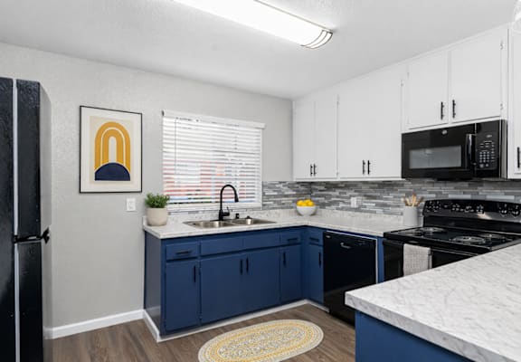 A kitchen with blue cabinets and a black refrigerator.