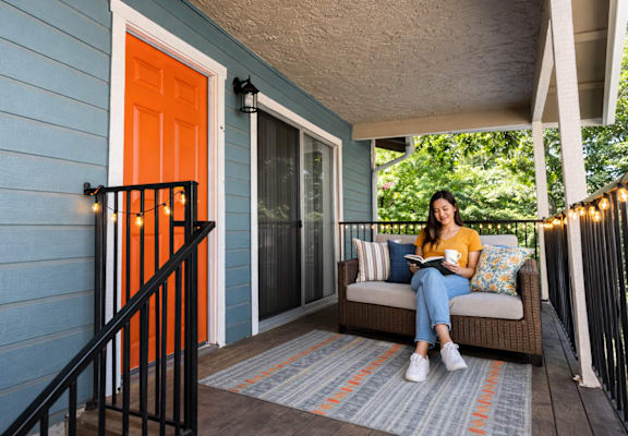 Woman sitting on wooden deck on couch at Redwood Cove Apartments, Chico