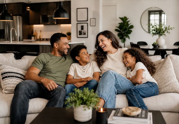 A family of four is sitting on a couch in a well-lit living room.
