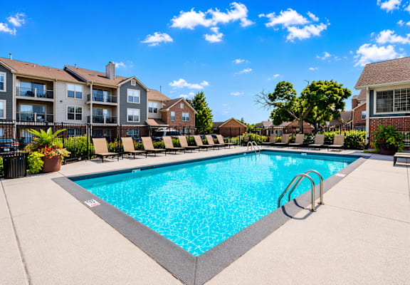 A swimming pool surrounded by lounge chairs and apartment buildings.