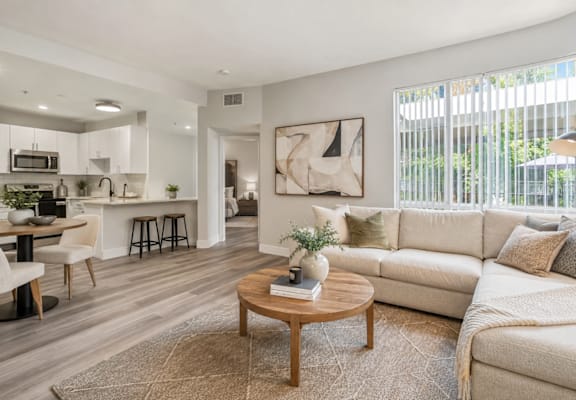 A modern living room with a white sofa, wooden coffee table, and a kitchen area in the background.