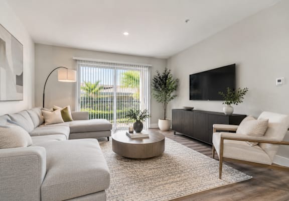 A modern living room with a grey sofa set, a wooden coffee table, and a flat-screen TV mounted on the wall.