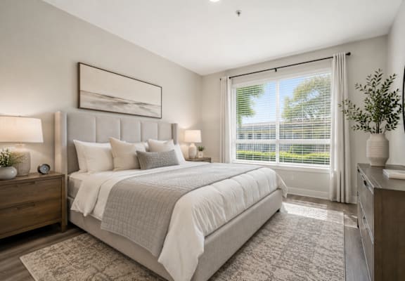 A well-lit bedroom with a large bed, two nightstands, and a window with blinds.