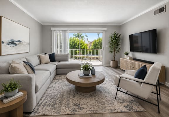 A living room with a white sofa, a wooden coffee table, a flat screen TV, and a large window with a view of a balcony.