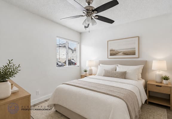 A well-lit bedroom with a large bed, a ceiling fan, and a small table with a plant on it.