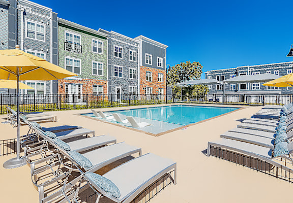 A pool area with sun loungers and umbrellas in front of a building.