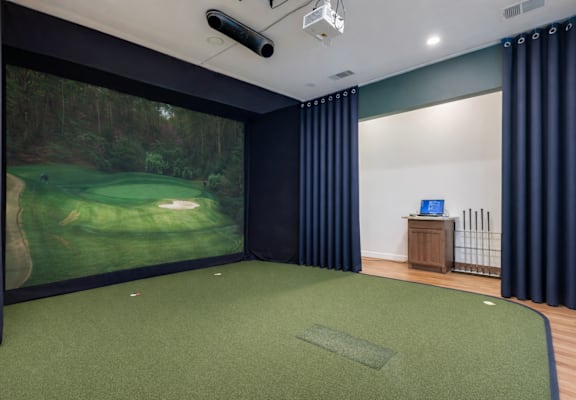 A room with a golf simulator and a green carpet.