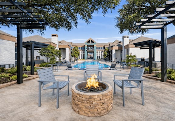 A fire pit sits in the middle of a patio with chairs around it.