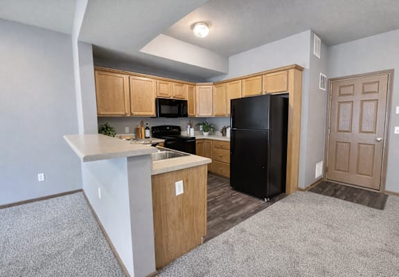 A kitchen with a black refrigerator and wooden cabinets.