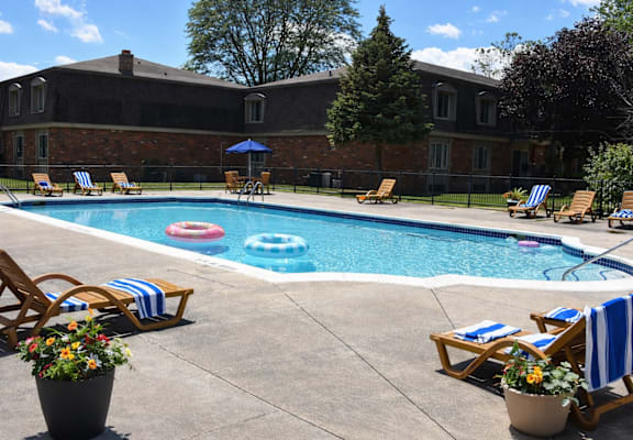A pool surrounded by chairs and umbrellas with a building in the background.