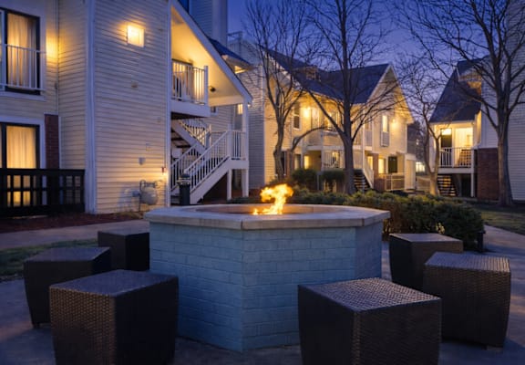 A fire pit in the middle of a courtyard surrounded by wicker chairs.