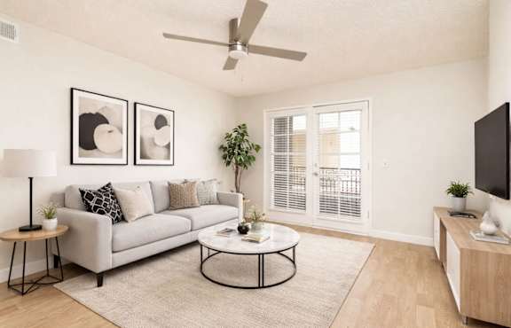 A living room with a grey couch, a coffee table, a ceiling fan, and a flat screen TV.