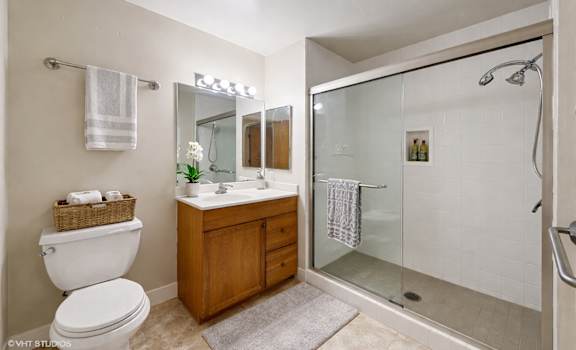 A bathroom with a toilet, sink, mirror, and shower.