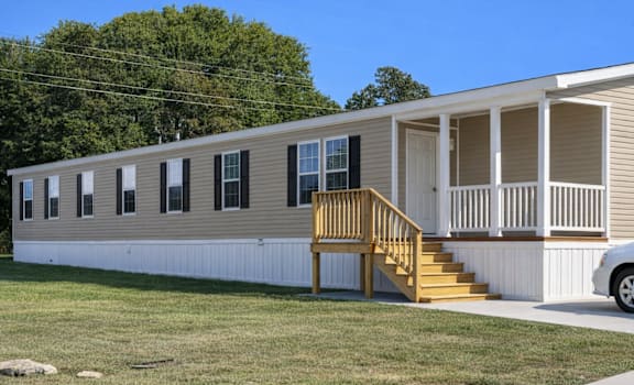 A mobile home with a porch and a car parked in front.