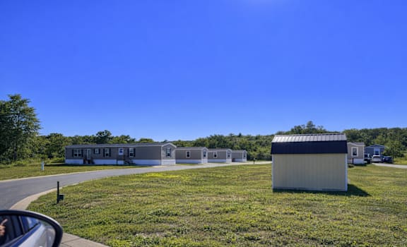 A sunny day at a grassy field with a building and a car in the foreground.