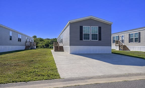 A house with a grey siding and a white trim is surrounded by a grassy area and other similar houses.
