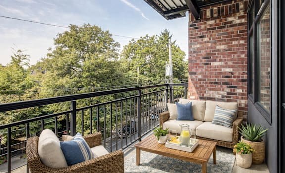 A balcony with a sofa, wicker chair, and a coffee table with a tray of food on it.