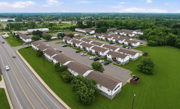 A road runs through a grassy area next to a large housing development.