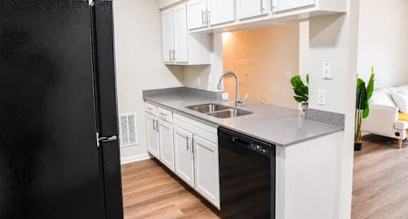 A black refrigerator stands in a kitchen with white cabinets and a black dishwasher.