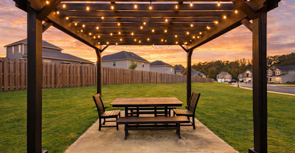 A wooden pergola with lights is set up in a backyard.