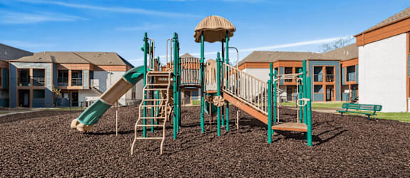 A playground with a green slide and a brown sandbox.