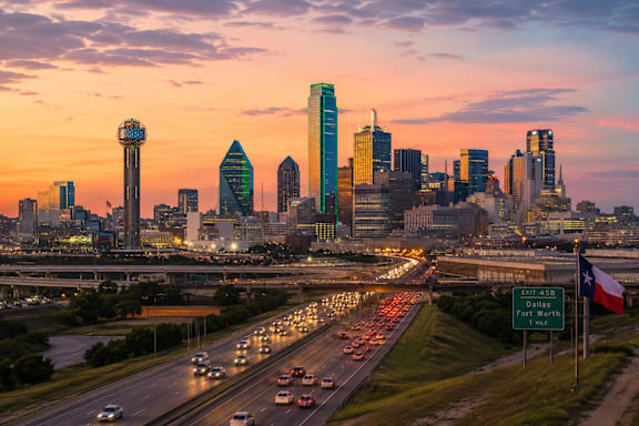 A city skyline at sunset with a highway in the foreground.