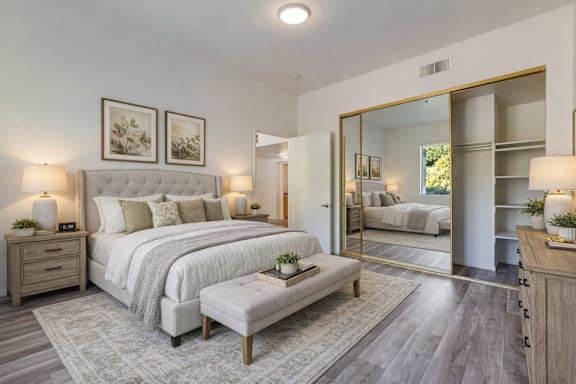 A bedroom with a large bed, a bench, and a mirror.
