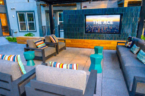 A modern outdoor seating area with a television screen displaying "THE ACE".