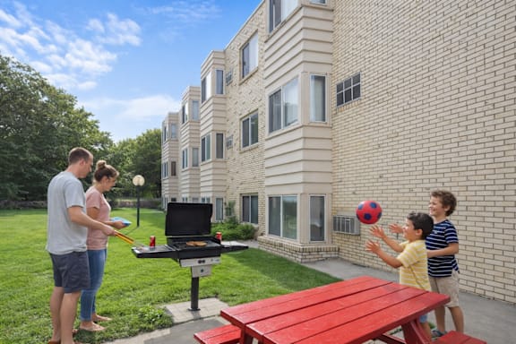 A BBQ grill is on a patio in front of a brick building.