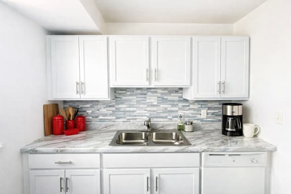 A kitchen with white cabinets and a marble countertop.