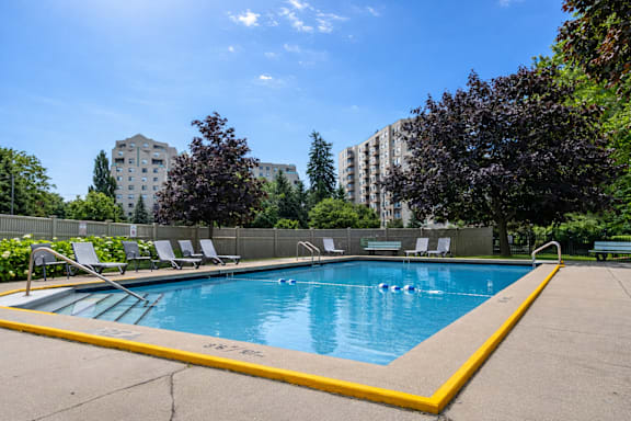 A swimming pool surrounded by trees and chairs.
