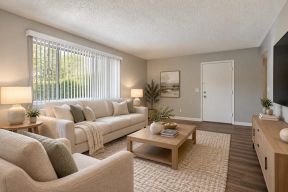 A living room with a white sofa, a wooden coffee table, and a large window with blinds.