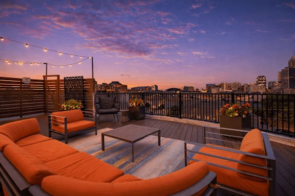 a balcony with orange chairs and a couch with lighting overlooking downtown indianapolis 