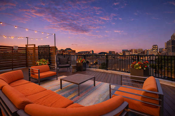 a balcony with orange chairs and a couch with lighting overlooking downtown indianapolis 