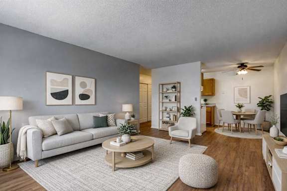 A living room with a white couch, a grey rug, a wooden coffee table, and a dining table with chairs.
