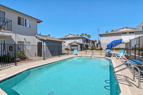 A swimming pool surrounded by a black fence and blue lounge chairs.