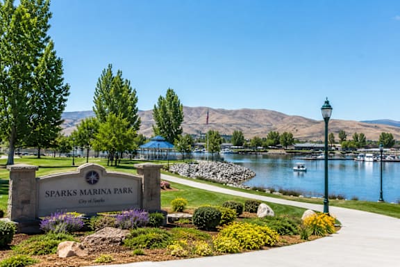 A sign for Sparks Marina Park is in the foreground of a park with a lake and mountains in the background.
