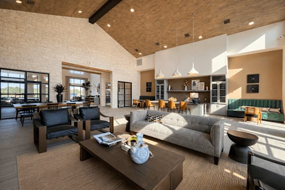 Spacious apartment resident lounge with high ceilings, comfortable seating, kitchen island, dining table, and natural light.