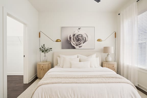 A bedroom with a large bed, two lamps, and a painting on the wall.