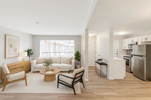 A modern living room with a white sofa, a wooden coffee table, and a kitchen in the background. at The Park on 13 Apartments - Royal Oak, MI Apartments, Royal Oak, MI, 48073