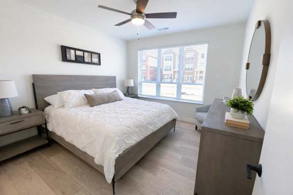 A bedroom with a large bed, a ceiling fan, and a window with a view of a building outside.