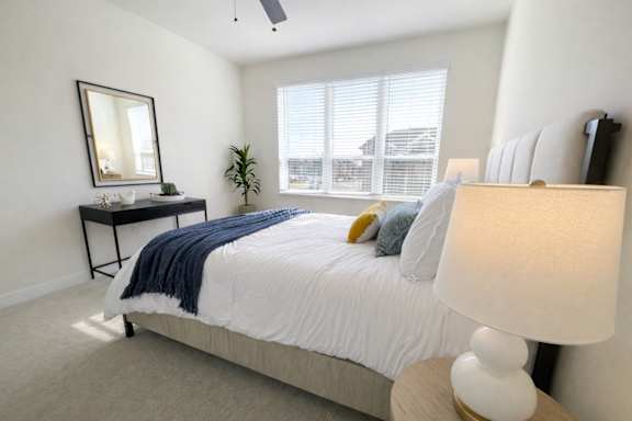 A bedroom with a bed, nightstand, and a window with blinds.