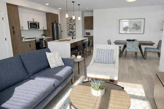 A grey couch sits in a well-lit living room with a dining area in the background.