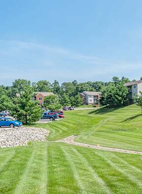 A grassy field leads to a building with a parking lot in front.