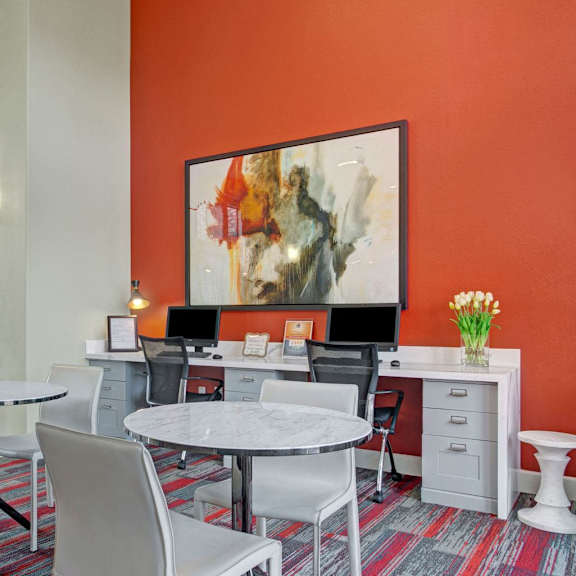 The community room with tables and chairs and desks with desktop computers and chairs at Mirador Apartments. 